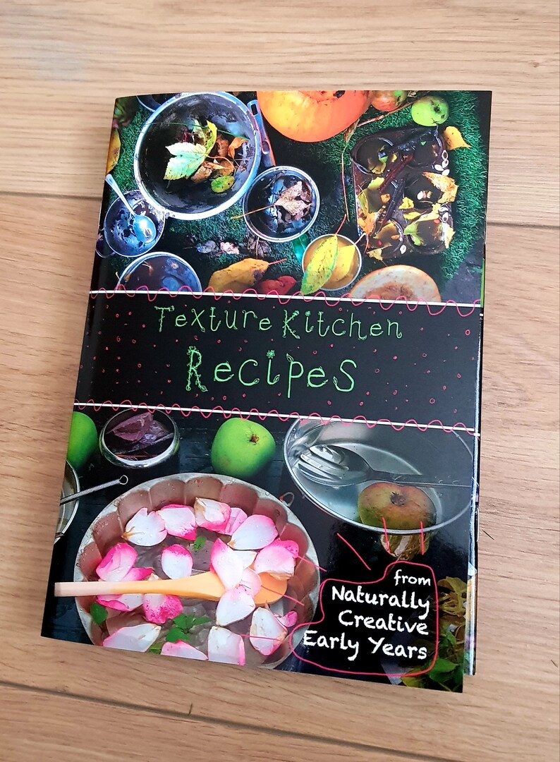 Puede incluir: Una portada de libro en blanco y negro con el t&iacute;tulo "Texture Kitchen Recipes" en letras verdes y rosas. La portada presenta una variedad de im&aacute;genes de comida y naturaleza, incluyendo manzanas, hojas y un taz&oacute;n de p&eacute;talos de rosa. El libro es de "Naturally Creative Early Years".