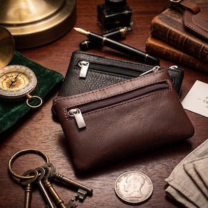 Könnte beinhalten: Zwei rechteckige Reißverschlusstaschen, eine in Dunkelbraun und eine in Schwarz, mit einer glatten Textur bei der braunen Tasche und einer genarbten Struktur bei der schwarzen. Jede Tasche hat einen silberfarbenen Metallreißverschluss und ein Fach.