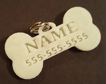 May include: White plastic dog bone tag with the text "NAME" and a phone number "555-555-5555" engraved on it.