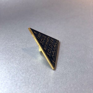 May include: Black triangle-shaped enamel pin with gold trim. The pin features the text "I got a soul but I'm not a soldier" in a white font.