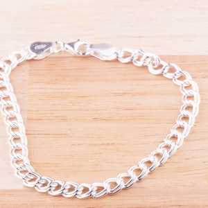 May include: A silver chain bracelet with a curb link design. The bracelet is made of sterling silver and has a polished finish.