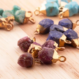 May include: Assortment of gemstone pendants with gold-toned accents. The pendants feature various colours, including teal, blue, and purple.