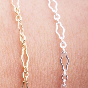 May include: Two chains, one gold and one silver, with a wavy, open link design. The chains are lying on a person's arm.