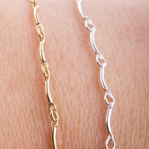 May include: Two chain bracelets, one gold and one silver, with a wavy link design.