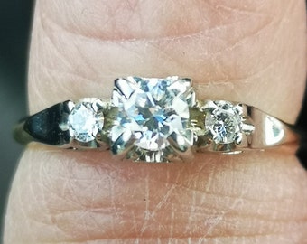 Puede incluir: Un anillo de plata con tres diamantes redondos. El diamante central es más grande que los dos diamantes laterales.