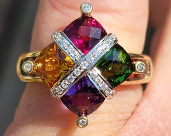 May include: A gold ring featuring a central design of four colorful, square-cut gemstones: red, orange, green, and purple. A white gold X-shaped band, encrusted with small diamonds, crosses the center. Small diamonds are set on the ring's band.
