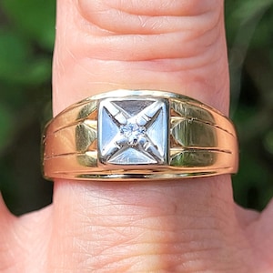 May include: A gold ring with a square-shaped setting featuring a single diamond in the centre.