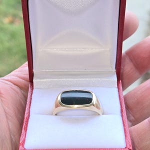 May include: A gold ring with a dark green and red gemstone in a red ring box.