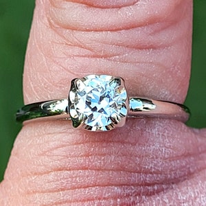 May include: A silver ring with a round, clear gemstone set in a prong setting.