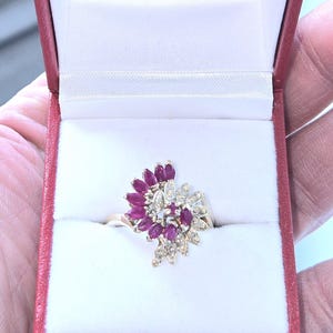 Peut inclure: Une bague en or avec un groupe de rubis rouges et de diamants blancs sertis dans un motif floral.