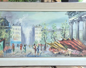 May include: Oil painting of a European city scene with figures walking on a cobblestone street. The artwork features buildings, trees, and a classical architectural element. The painting is framed in a white wooden frame.