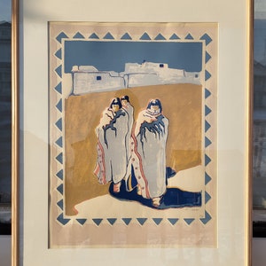 Könnte beinhalten: Ein gerahmter Druck eines farbenfrohen Kunstwerks, das drei Figuren in traditioneller Kleidung zeigt, die vor einem Dorf stehen. Die Figuren tragen blaue, weiße und rote Kleidung. Das Dorf befindet sich im Hintergrund und ist in Weiß-, Blau- und Brauntönen gemalt. Das Kunstwerk ist in einem hellen Holzrahmen gerahmt.