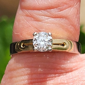 May include: A gold and silver ring with a single round diamond in the center.