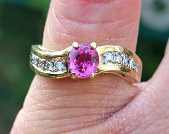 Può includere: Un anello d'oro con una pietra preziosa rosa circondata da pietre preziose più piccole e trasparenti.
