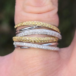 Könnte beinhalten: Ein Stapel von fünf Ringen mit abwechselnden Bändern aus gelben und weißen Diamanten. Die Ringe werden an einem Finger getragen.