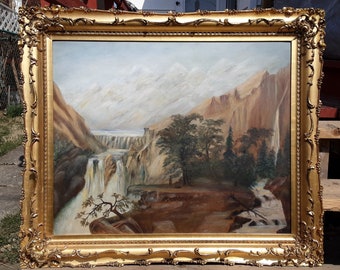 May include: A framed oil painting depicting a waterfall cascading down a mountainside. The painting features a lush green forest in the foreground and snow-capped mountains in the background. The painting is framed in a gold-colored frame.