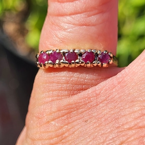 May include: A gold band ring with five red gemstones set in a row.