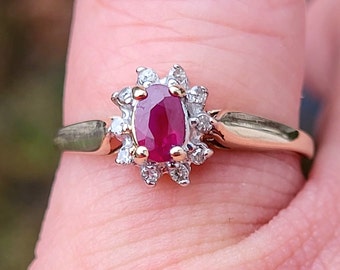 Pode incluir: Um anel de ouro com uma gema oval de rubi vermelho cercada por um halo de diamantes menores.