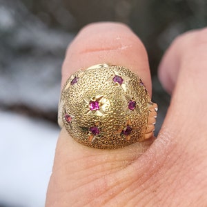 Puede incluir: Un anillo de oro con una superficie texturizada y piedras preciosas rosas engastadas en forma de estrella.