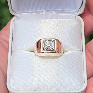 May include: A gold ring with a square-shaped diamond in the center. The ring is in a white ring box.