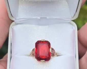 May include: A red gemstone ring with a gold band. The ring is in a white ring box.