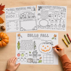 May include: Three white paper placemats with black line art for colouring, featuring autumn themes like pumpkins, scarecrows, and corn. The sheets include activities such as mazes, counting games, and drawing prompts. One sheet is partially coloured with orange.