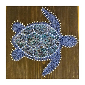 May include: A blue and white string art piece depicting a sea turtle on a dark brown wooden background.