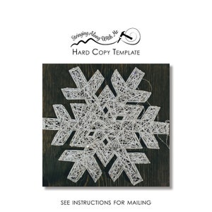 May include: A white string art snowflake design on a dark wood background. The design is intricate and detailed, with many lines and curves. The snowflake is centered in the image, and the background is a dark brown wood.