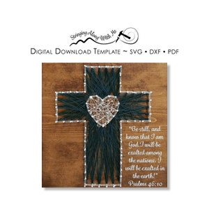 May include: A string art cross with a heart in the center. The cross is made with dark blue string and the heart is made with white string. The background is a brown wooden surface. The text "Be still, and know that I am God. I will be exalted among the nations, I will be exalted in the earth!" is written below the cross. The text "Psalms 46:10" is written below the quote.