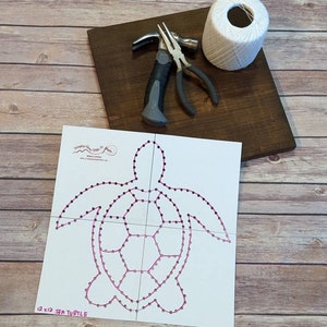 May include: A white wooden board with a white string wrapped around a spool, a hammer, and pliers. A white paper template with a pink outline of a sea turtle with the text "12 x 12 SEA TURTLE" is on top of the board.