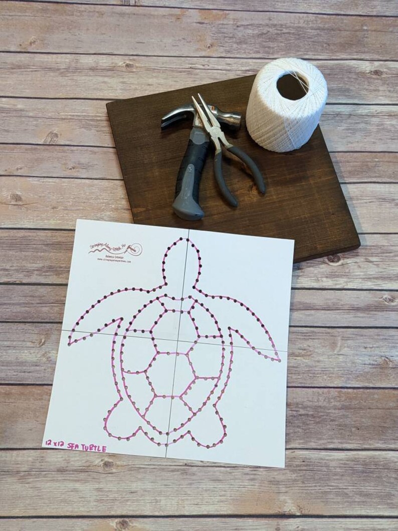 May include: A white wooden board with a white string wrapped around a spool, a hammer, and pliers. A white paper template with a pink outline of a sea turtle with the text "12 x 12 SEA TURTLE" is on top of the board.