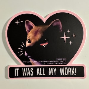 May include: A sticker with a pink heart-shaped border featuring a dog's face against a black background. The text "IT WAS ALL MY WORK!" is displayed on a black rectangle at the bottom. The sticker also includes copyright information.