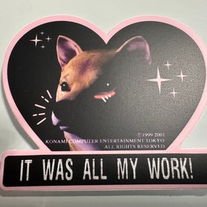 May include: A heart-shaped sticker featuring a Shiba Inu dog with a black background and pink border. The sticker has the text "IT WAS ALL MY WORK!" at the bottom. The sticker also includes the text "KONAMI COMPUTER ENTERTAINMENT TOKYO ALL RIGHTS RESERVED."