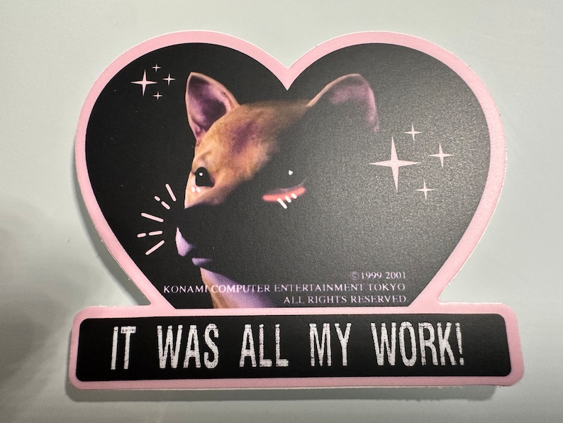 May include: A heart-shaped sticker featuring a Shiba Inu dog with a black background and pink border. The sticker has the text "IT WAS ALL MY WORK!" at the bottom. The sticker also includes the text "KONAMI COMPUTER ENTERTAINMENT TOKYO ALL RIGHTS RESERVED."