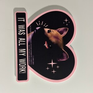 May include: A sticker with a pink heart shape and a black background featuring a dog's face. The sticker has the text "IT WAS ALL MY WORK!" in white, and the copyright information for Konami Computer Entertainment Tokyo.