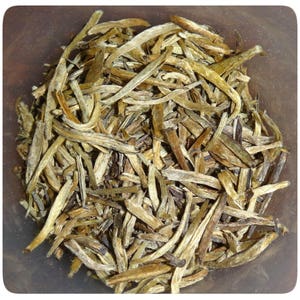 May include: Loose leaf white tea with long, thin, dried leaves in shades of brown and beige.