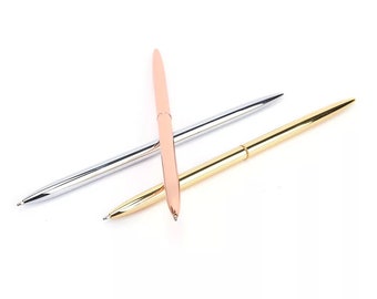 May include: Three slim, metallic ballpoint pens arranged in a cluster. One pen features a polished silver finish, another has a warm rose gold tone, and the third is finished in a bright, reflective gold colour. Each pen has a tapered point.