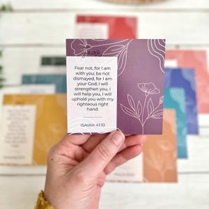 May include: A hand holding a square card with the word "Fear" and a floral design. The card has a quote from Isaiah 41:10. Other cards with different colors and designs are in the background.