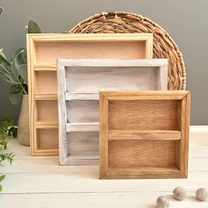 May include: Three square wooden display shelves arranged in a tiered formation. The largest shelf is natural light wood, the middle shelf has a distressed white painted finish, and the smallest front shelf is a medium brown stained wood.