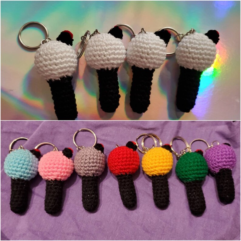 May include: A collection of crochet microphone keychains in various colors. The microphones have a white or colored ball-shaped top, a black handle, and a silver keyring. The keychains are displayed on a reflective surface and a purple fabric.