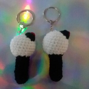 May include: Two handmade crochet keychains. Each keychain features a white, spherical top with a black base and a small red accent. The keychains are attached to silver-colored key rings.