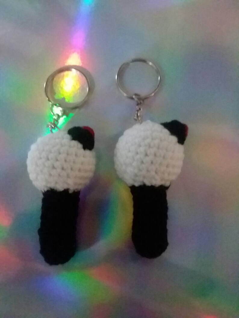 May include: Two handmade crochet keychains. Each keychain features a white, spherical top with a black base and a small red accent. The keychains are attached to silver-colored key rings.