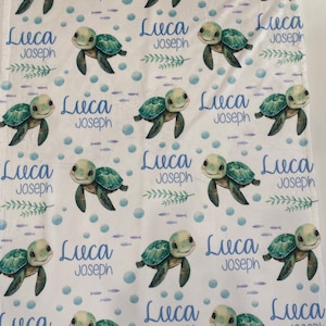 May include: White baby blanket with a repeating pattern of green sea turtles, blue bubbles, and the name Luca Joseph in blue text.