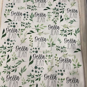 May include: White baby blanket with a green leafy pattern and the name "Della Jean" repeated throughout.