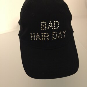 May include: Black baseball cap with the words "BAD HAIR DAY" spelled out in rhinestones.
