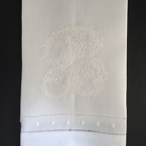 May include: White hand towel with a delicate embroidered floral design. The towel has a scalloped edge with small embroidered dots.