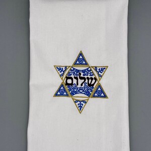 May include: White kitchen towel with a blue and gold embroidered Star of David with the Hebrew word "Shalom" in the center.