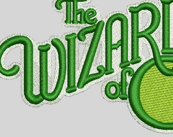 May include: Embroidered patch featuring the text "The Wizard of Oz" in green, with a white outline. The design includes a green circle for the "O" in "Oz". The patch is on a light gray background.