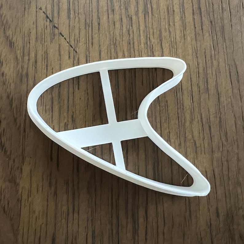 以下が含まれることがあります： 内側にクロスハッチデザインが施されたブーメラン型の白いプラスチック製のクッキーカッターです。