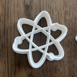 以下が含まれることがあります： 原子形の白いプラスチック製のクッキーカッター。カッターは、複数の層を持つ詳細なデザインです。